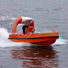 Orange fast rescue boat with a crew member at the helm speeding across open water, leaving a white wake