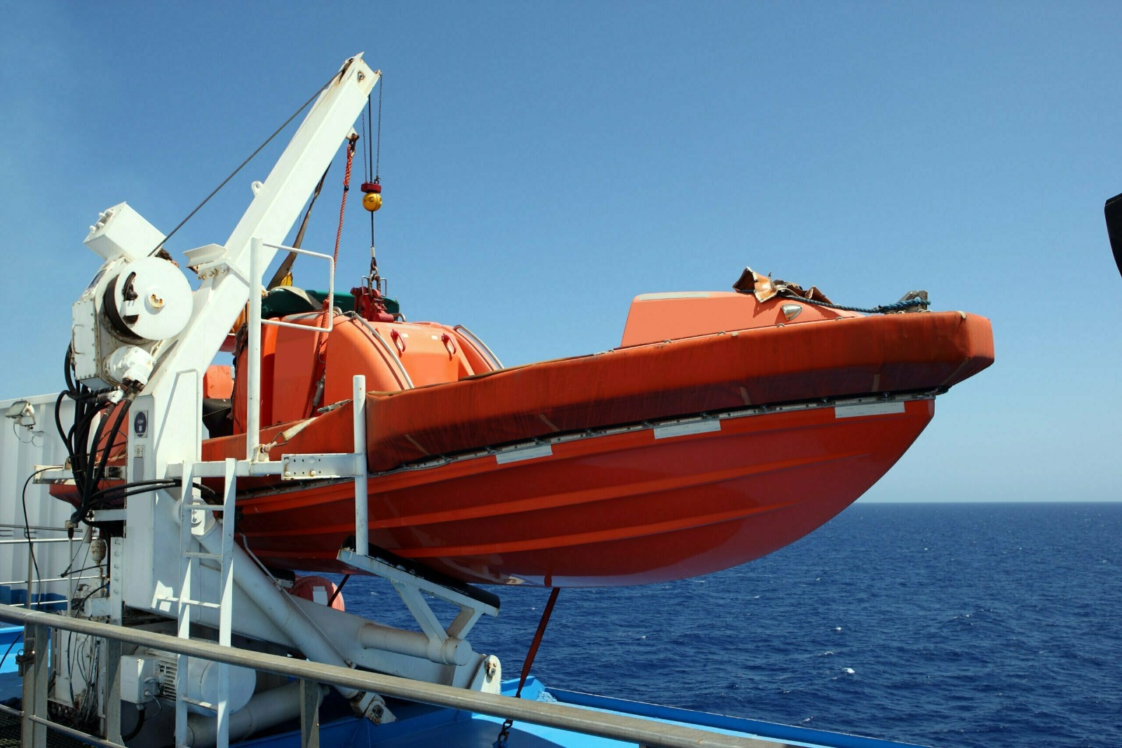 Orange lifeboat hanging from davits on the side of a ship.